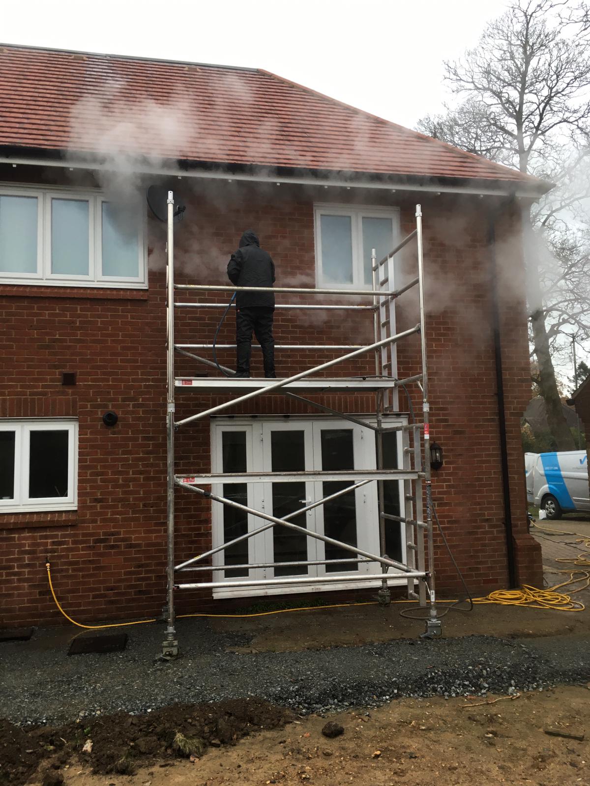 A man on scaffolding cleaning the bricks of a house