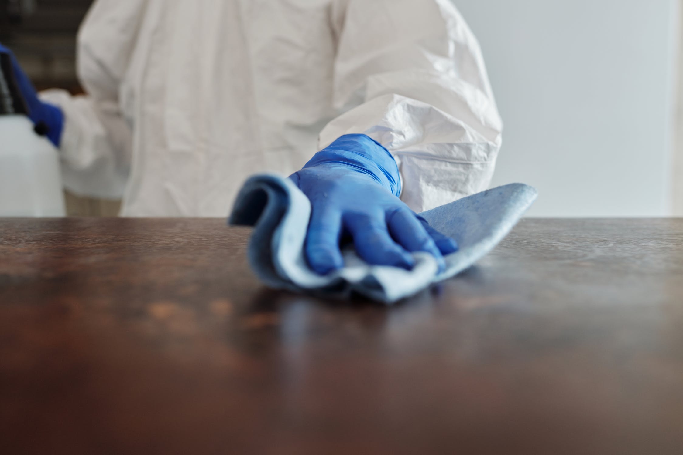 A gloved hand wiping down a wooden surface with a cloth to help illustrate Vinci Response's Hoarder Cleaning Services