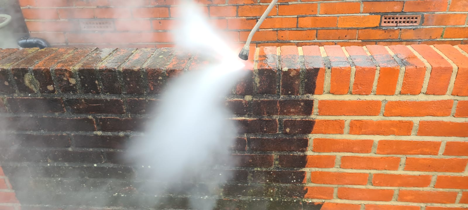 Cleaning a brick wall using a pressure washer, showing the improvement of the wall before compared to after.