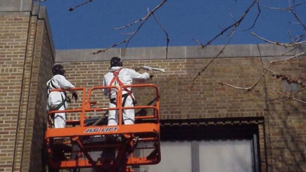 Two men dry ice blasting a brick wall.