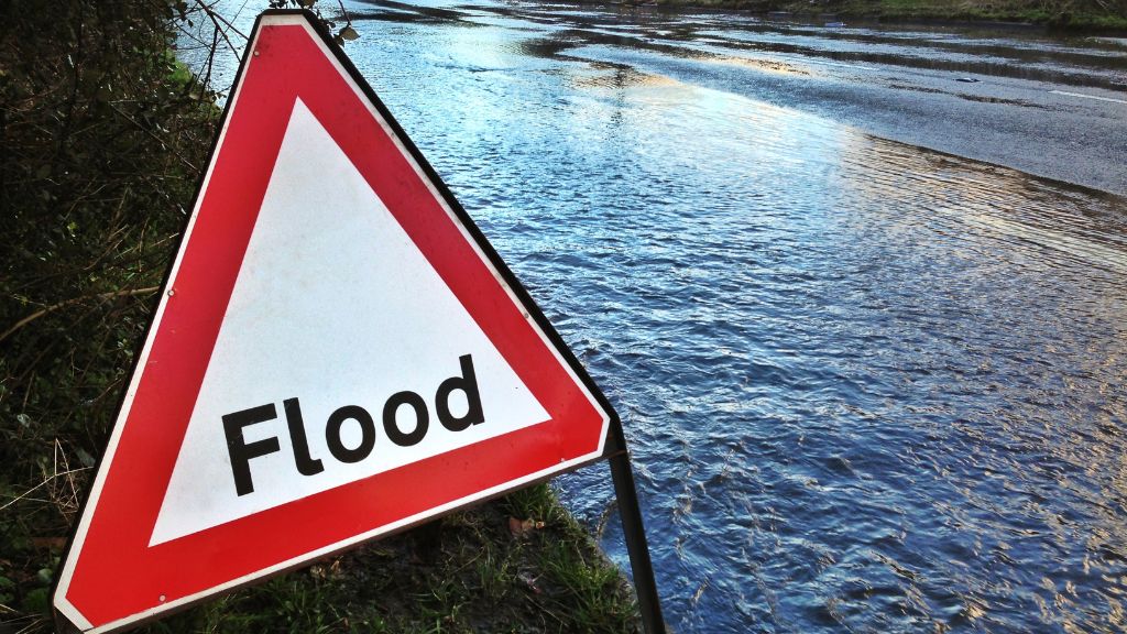 “Flood warning sign on a roadside next to rising flood water”