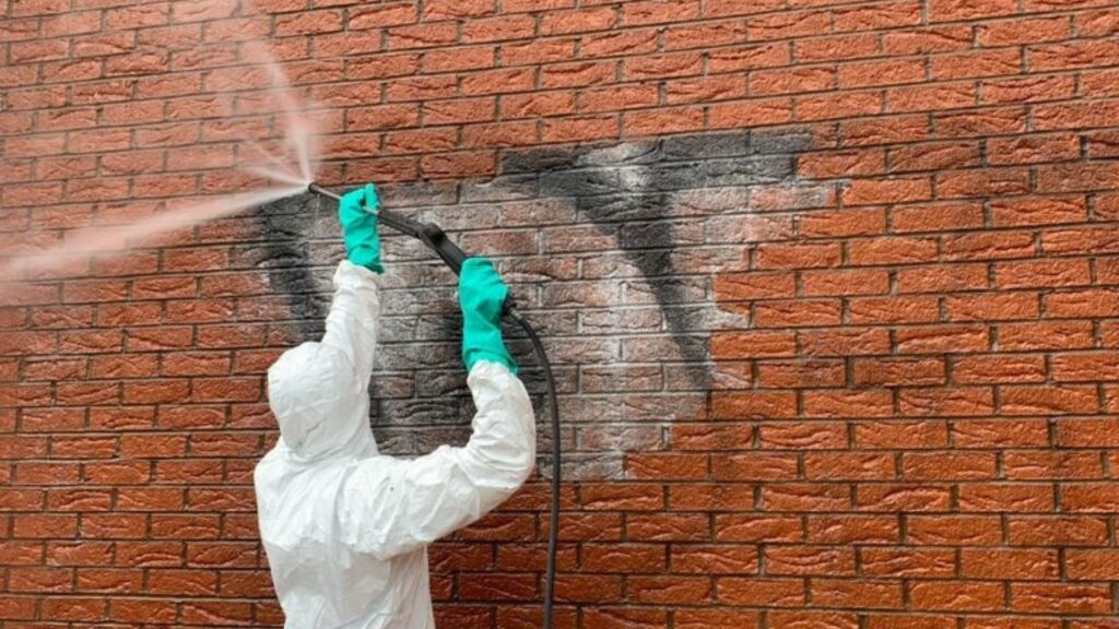 Torik steam cleaner being used to clean graffiti off a brick wall.