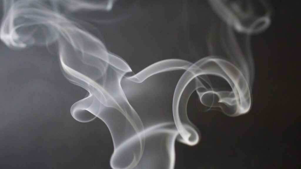 Wisps of white smoke spiralling upwards against a black background.