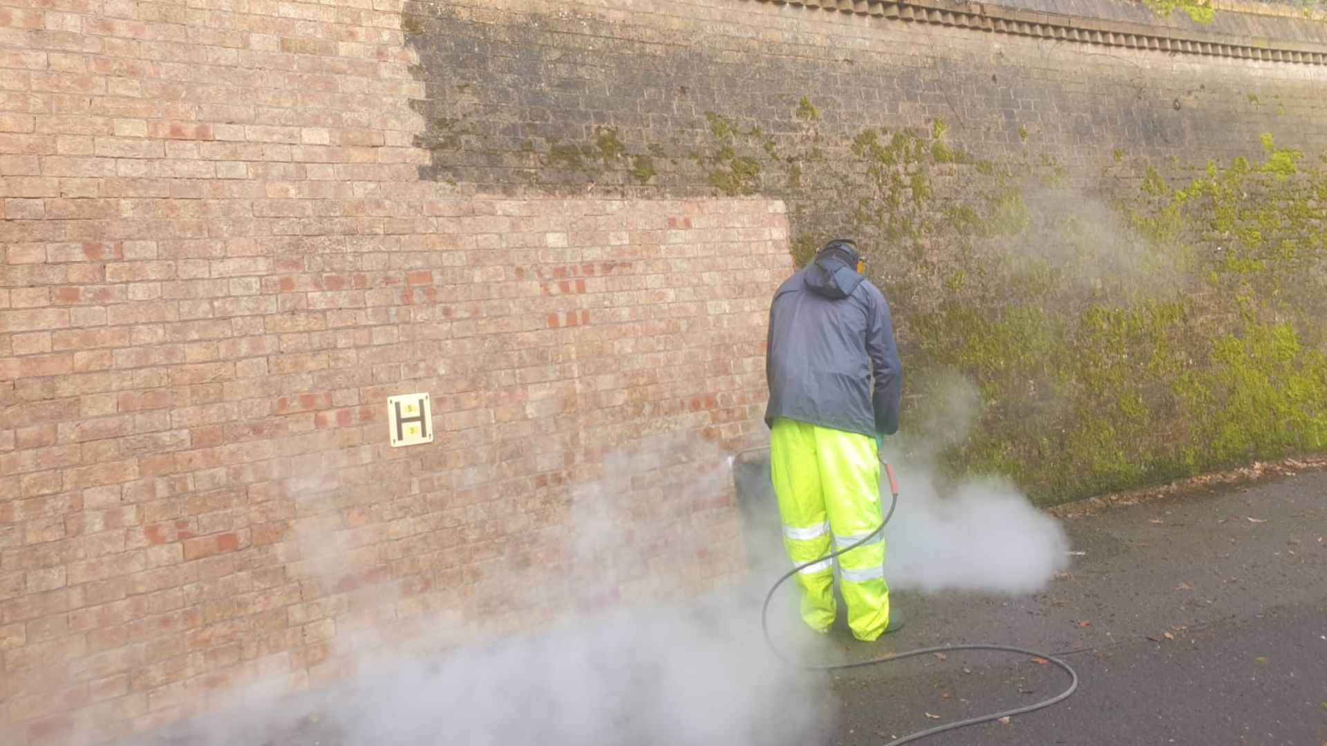 A man power washing dirt from a brick wall.