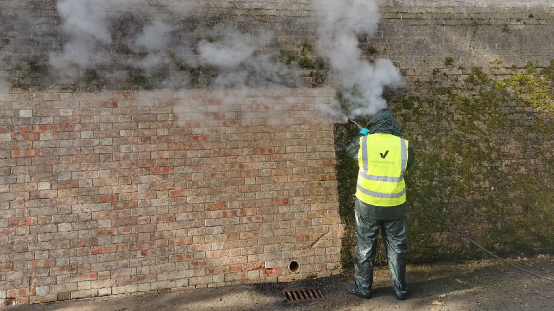 A man in a high visibility jacket continuing to clean a brick wall.