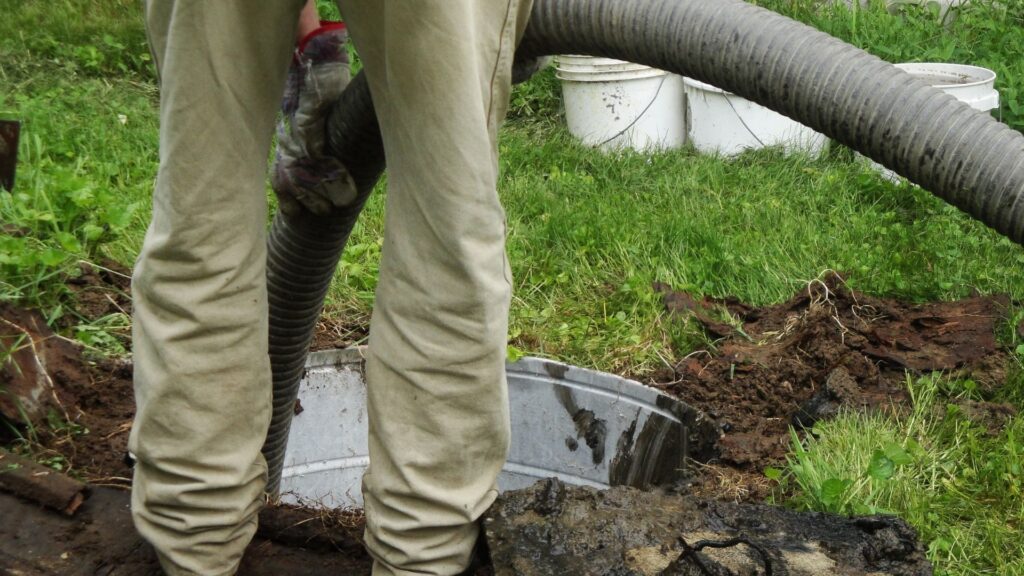 A man feeding a tube into an open septic tank to help illustrate the health hazards of leaking sewage.
