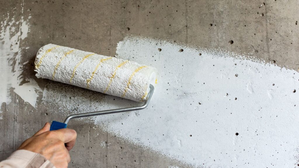 A hand holding a paint roller, painting over a smoke damaged wall.