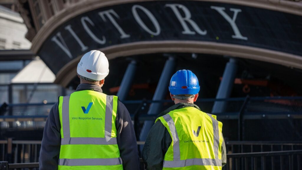 Two men in Vinci Response hi vis jackets looking at HMS Victory.