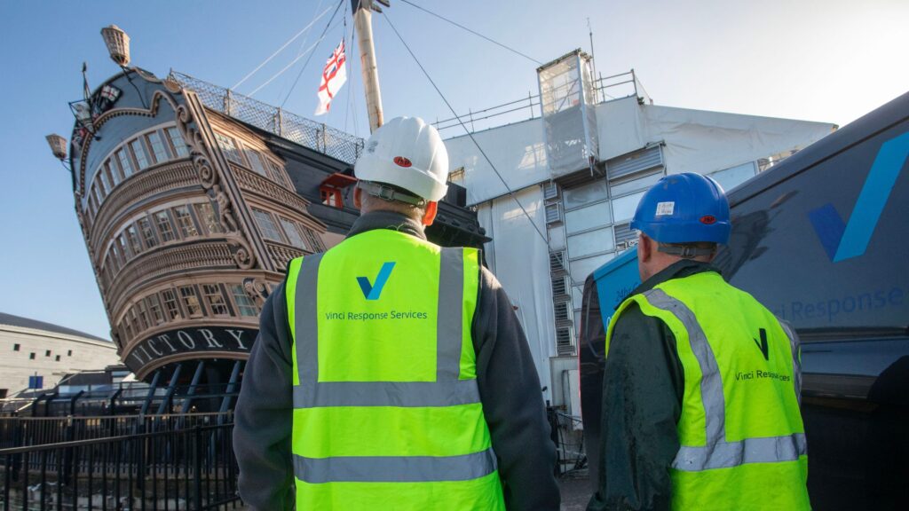 Two men in Vinci Response hi vis jackets looking at HMS Victory.