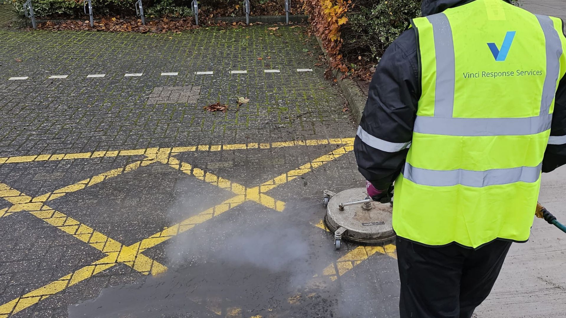A man wearing a Vinci Response-branded high visibility jacket cleaning bricks.