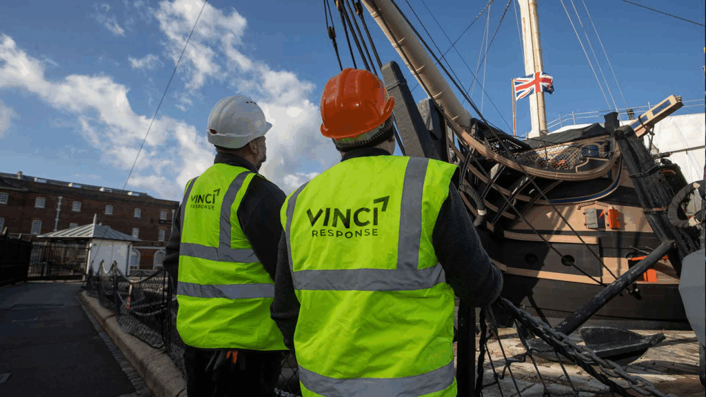 Two Vinci Response technicians chat and look up at HMS Victory.