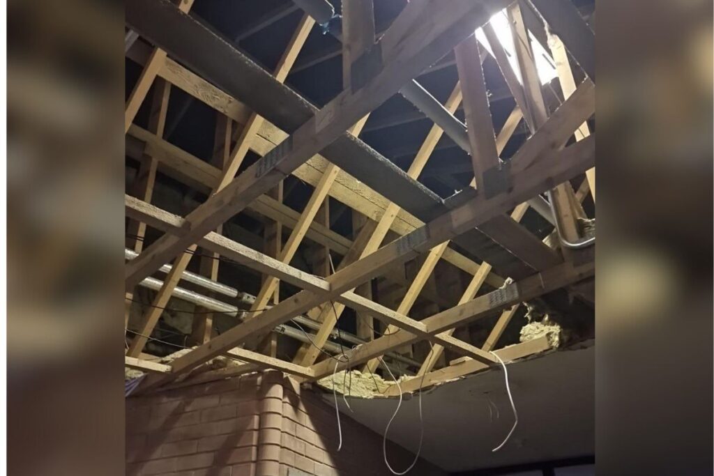 Exposed wooden roof trusses and insulation damage during structural inspection following water ingress.